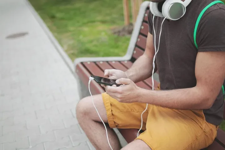 Bankta oturup kulaklıkla müzik dinleyen bir genç